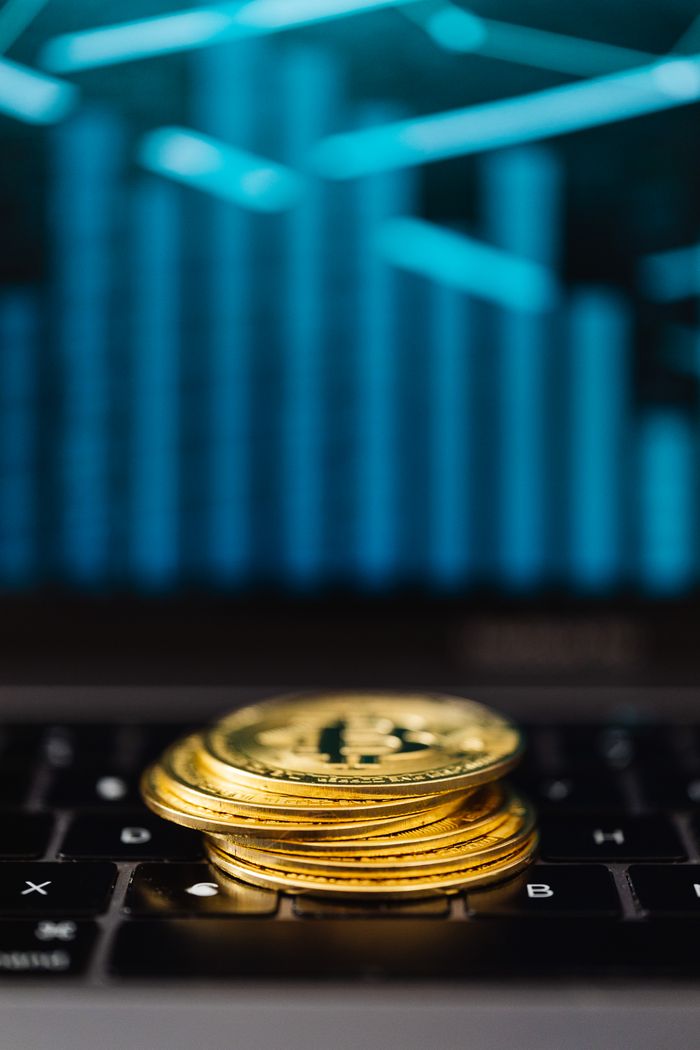 Services Close-up of gold Bitcoin coins stacked on a laptop keyboard with a digital chart reflection.