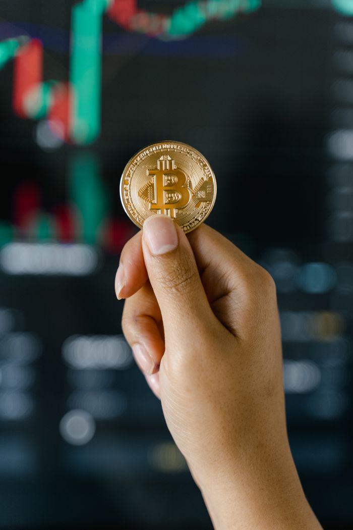 Services A hand holds a Bitcoin against a backdrop of financial charts, symbolizing cryptocurrency trading.
